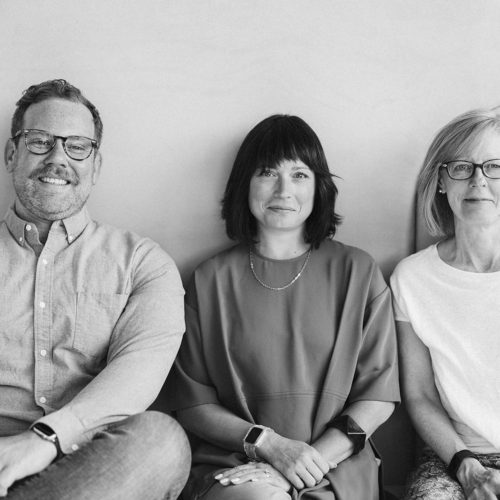 Black and white photo of City Thread team. From left to right Kyle (white man sitting down), Sara (white woman sitting down) and Zoe (white woman sitting down)