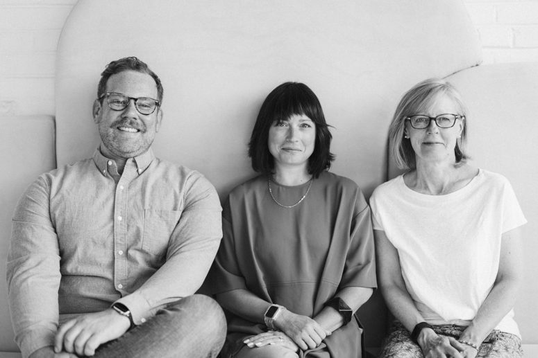 Black and white photo of City Thread team. From left to right Kyle (white man sitting down), Sara (white woman sitting down) and Zoe (white woman sitting down)